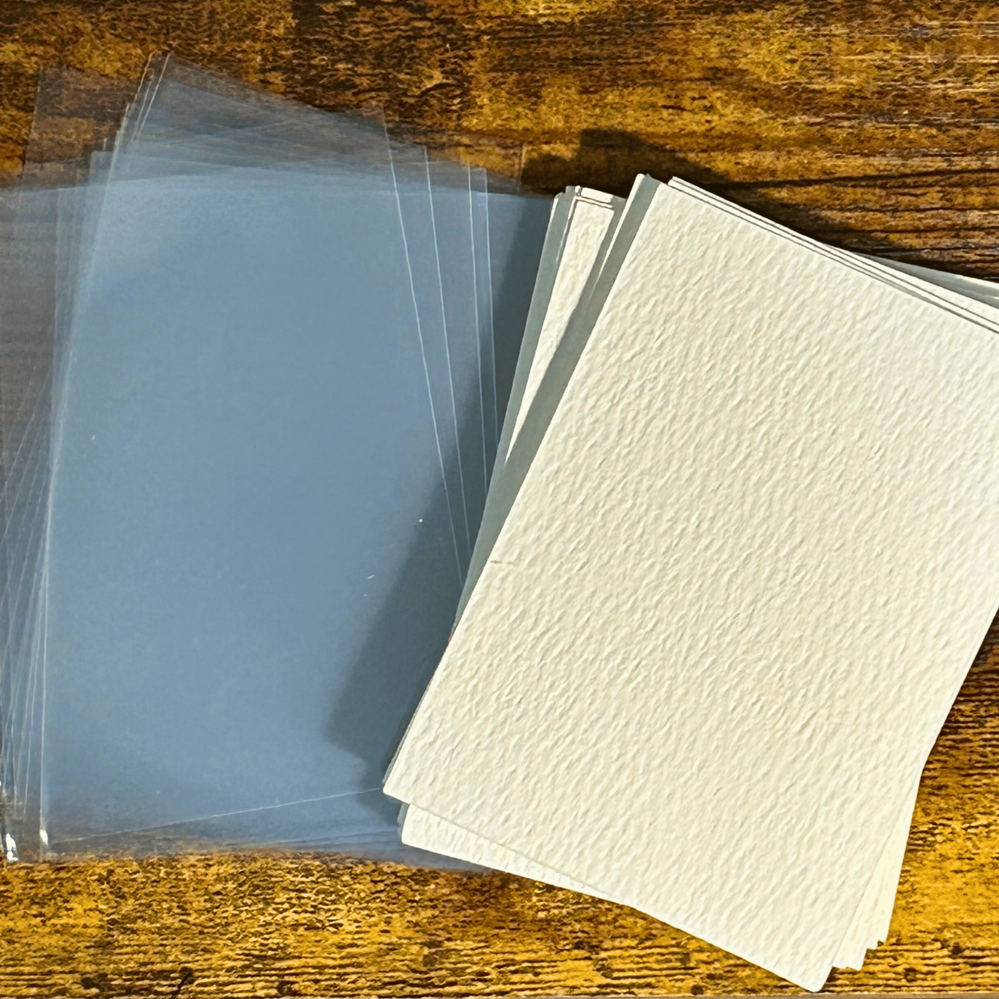 Clear and textured white watercolor paper sheets on a wooden surface