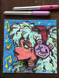 Colorful abstract painting on a small canvas with two markers on a wooden surface.